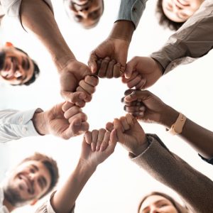 Teamwork, Power And Partnership Concept. Below view of multucultural group of smiling people making fist bump standing in circle. Workers doing fist pump together celebrating good deal